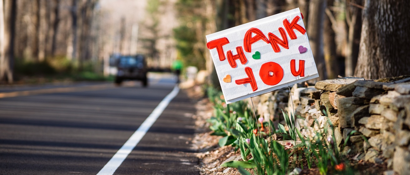 A handmade sign on the side of the road that reads "Thank you!" in red lettering