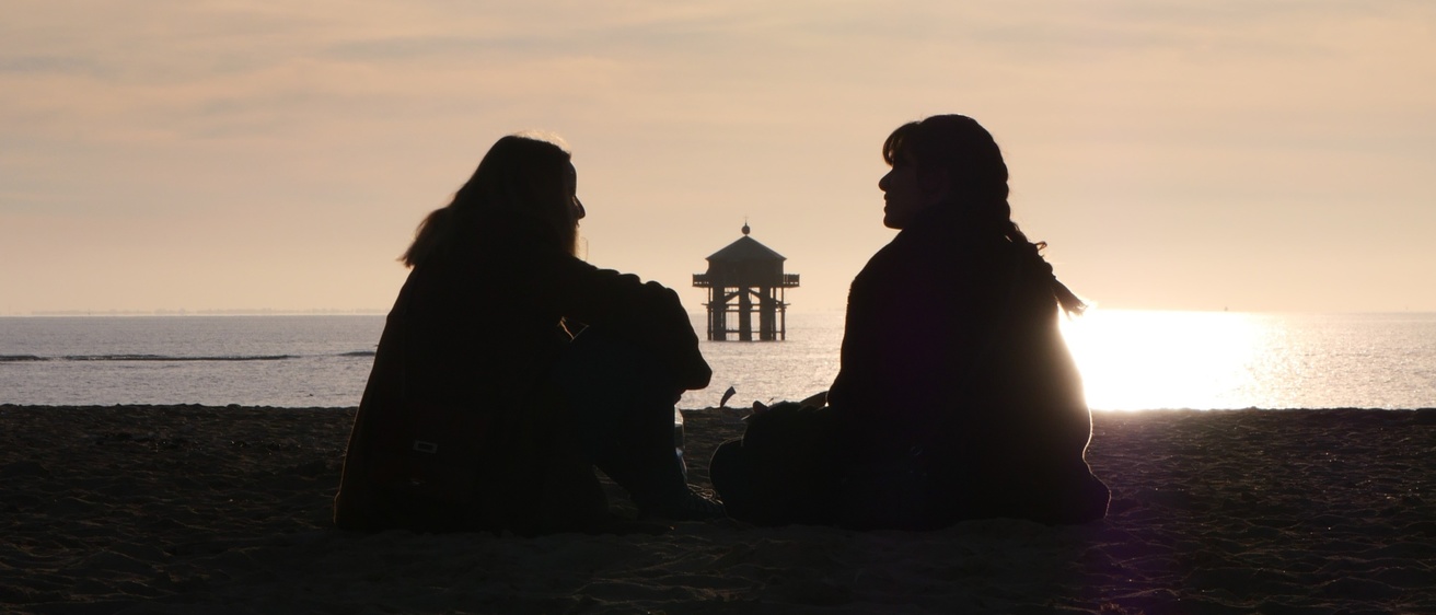 Two people sitting on a beach talking