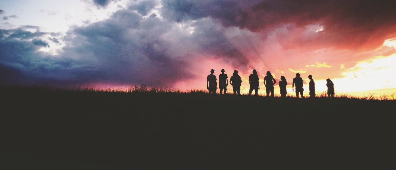 A group of people standing in front of a sunset
