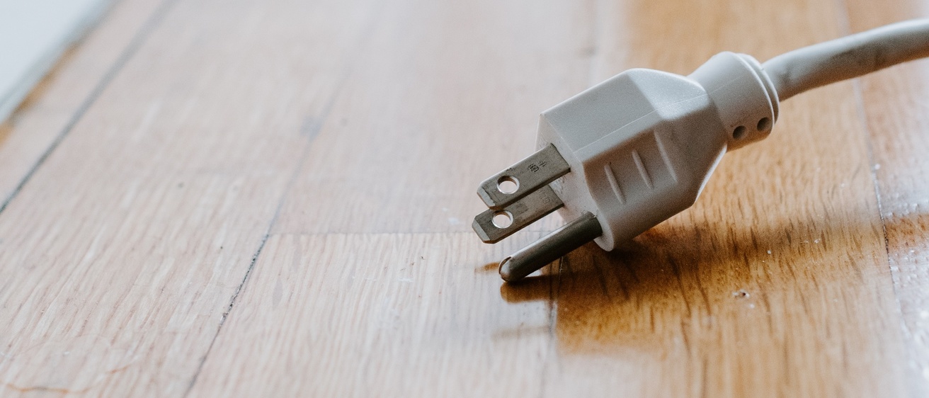 An electric plug unplugged and laying on a hardwood floor