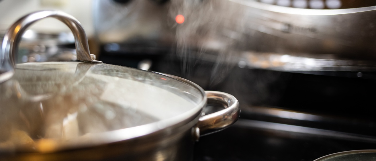 A pot on a stove with its contents steaming and nearly boiling