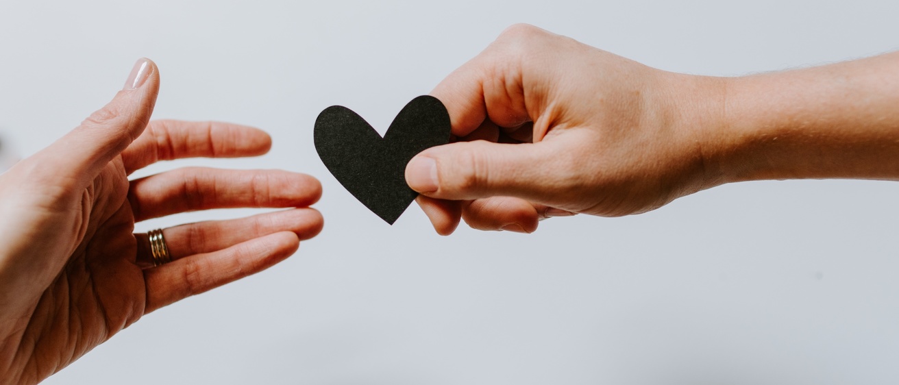 two hands reaching for a black paper heart