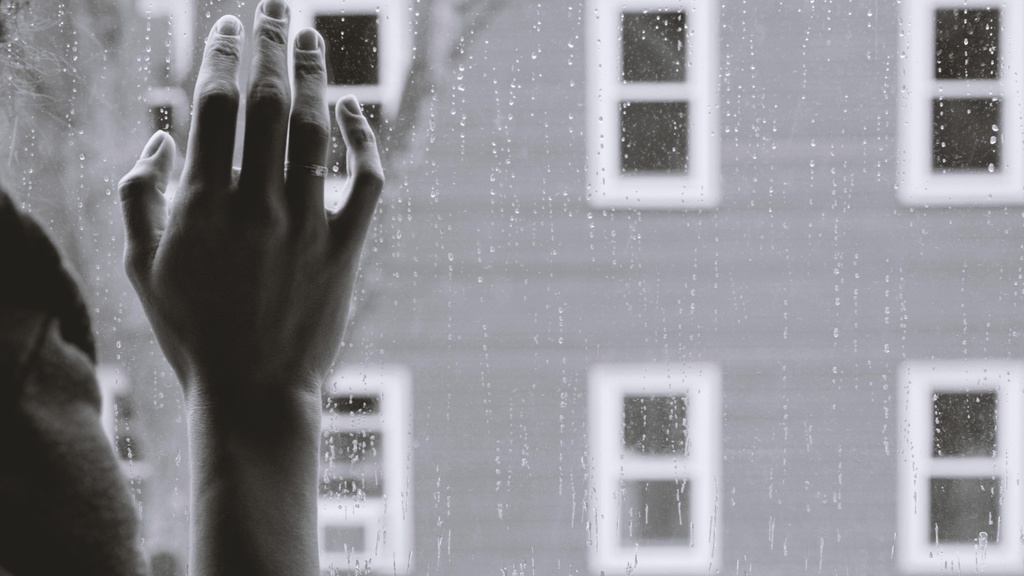 person with hand on window during rainy day