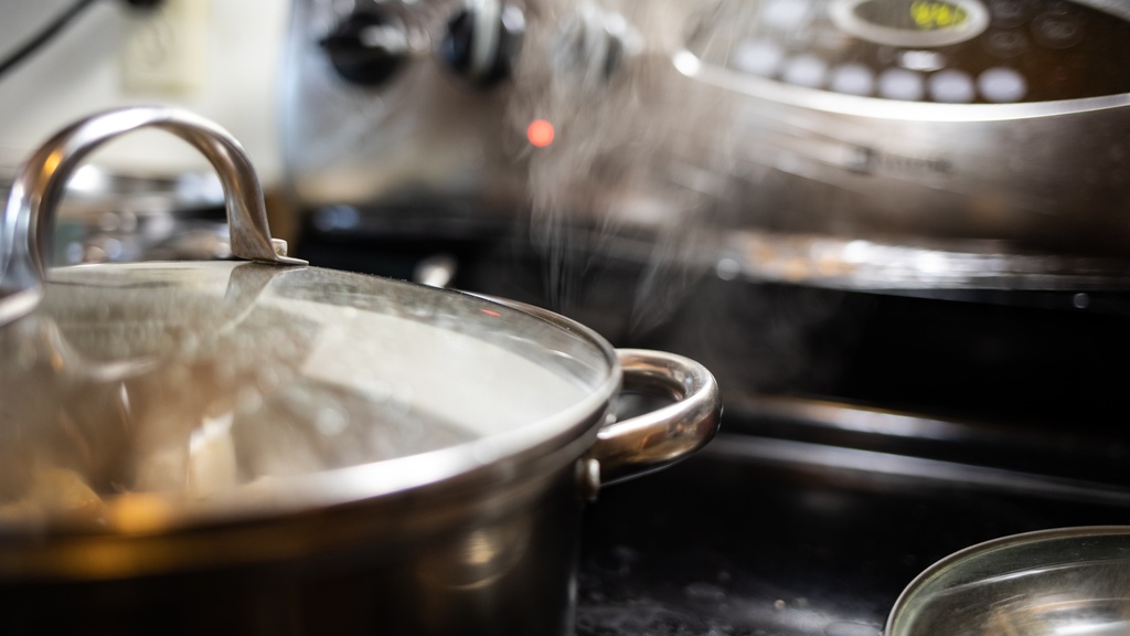 A pot on a stove with its contents steaming and nearly boiling