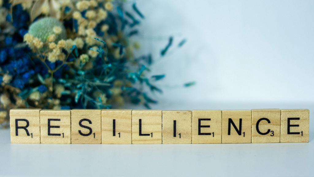 Scrabble letters arranged to spell "Resilience," placed in front of an arrangement of flowers